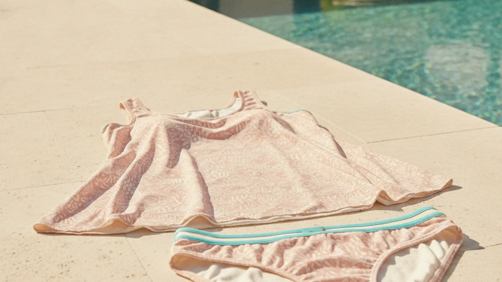 Femeie zâmbind, purtând un tankini modern pe plajă, cu un peisaj marin senin în fundal, sugerând confort și încredere după mastectomie.